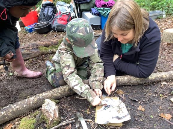 Teacher supervising a child to start a campfire