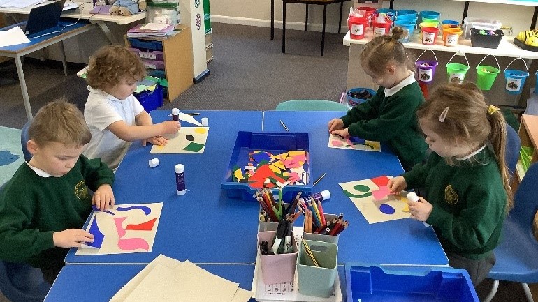 Four children sat around a table, gluing colourful shapes onto paper