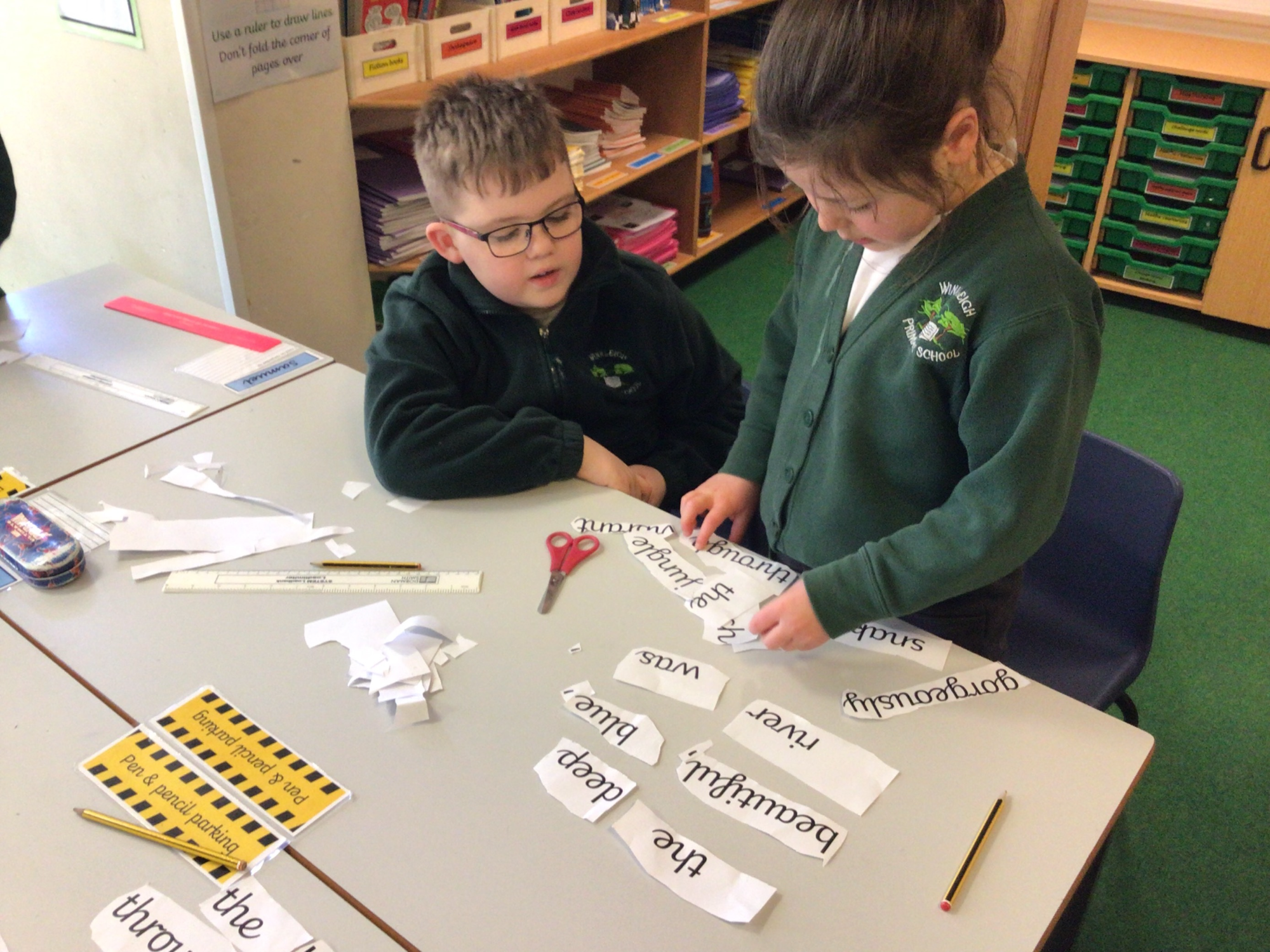 Two children using scissors to cut out words to make into sentences